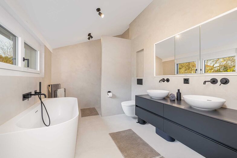 Das Badezimmer kommt ohne Fliessen aus und überzeugt mit einem dezenten Farbkonzept und schwarzen Armaturen.