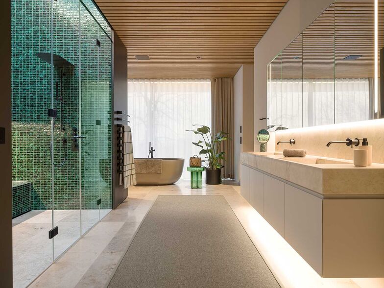 Hinter dem kompakten Einbaukörper aus Wandschränken und Wellnessdusche öffnet sich der Raum und führt zu der freistehenden Badewanne mit Ausblick ins Grüne.
