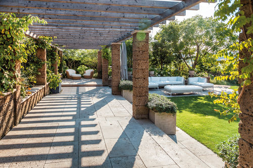 Rückzugsort mit Laubengang: Dieser Garten ist ein Ort der Ruhe und Entspannung. Eine lange Pergola mit Tuffsteinpfosten erstreckt sich wie ein Laubengang zum Loungebereich. Für den Plattenbelag wurde als Kontrastmaterial Muschelkalk gewählt. Vom Laubengang führt ein Tritt zur Rasenfläche und Lounge.