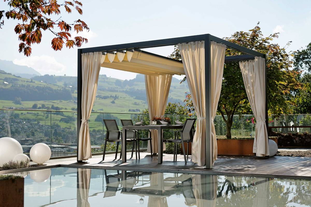 Von der Sonne, vor Wind und Regen geschützt: Dieser Essplatz wurde mit dem Gartenpavillon «Pergola» geschaffen: Ein Lieblingsplatz zum Verweilen. Das praktische PVC Schiebedach und die attraktiven Seitenvorhänge passen sich allen Wetteränderungen schnell an. Der Gartenpavillon kann bedenkenlos das ganze Jahr draussen stehen. Hunn Gartenmöbel.