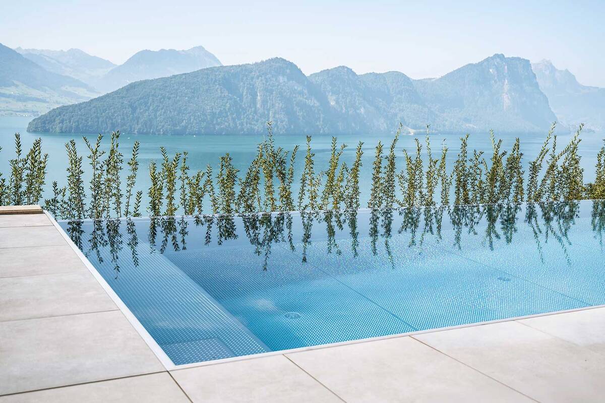 Der Edelstahl-Infinity-Pool mit den Massen 8 × 3,6 × 1,35 Meter fügt sich harmonisch in die Hanglage ein. Die Infinity-Rinne verschmilzt optisch nahtlos mit dem See und der Berglandschaft, während die schwebende Edelstahltreppe einen besonders leichten und modernen Einstieg ermöglicht. Mit hochwertiger Technik, effizienter Beheizung und einer Photovoltaikanlage, die den gesamten Energiebedarf mitversorgt, entstand ein Pool, der höchsten Ansprüchen an Ästhetik, Komfort und Nachhaltigkeit gerecht wird. Zireg.