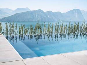 Der Edelstahl-Infinity-Pool mit den Massen 8 × 3,6 × 1,35 Meter fügt sich harmonisch in die Hanglage ein. Die Infinity-Rinne verschmilzt optisch nahtlos mit dem See und der Berglandschaft, während die schwebende Edelstahltreppe einen besonders leichten und modernen Einstieg ermöglicht. Mit hochwertiger Technik, effizienter Beheizung und einer Photovoltaikanlage, die den gesamten Energiebedarf mitversorgt, entstand ein Pool, der höchsten Ansprüchen an Ästhetik, Komfort und Nachhaltigkeit gerecht wird. Zireg.