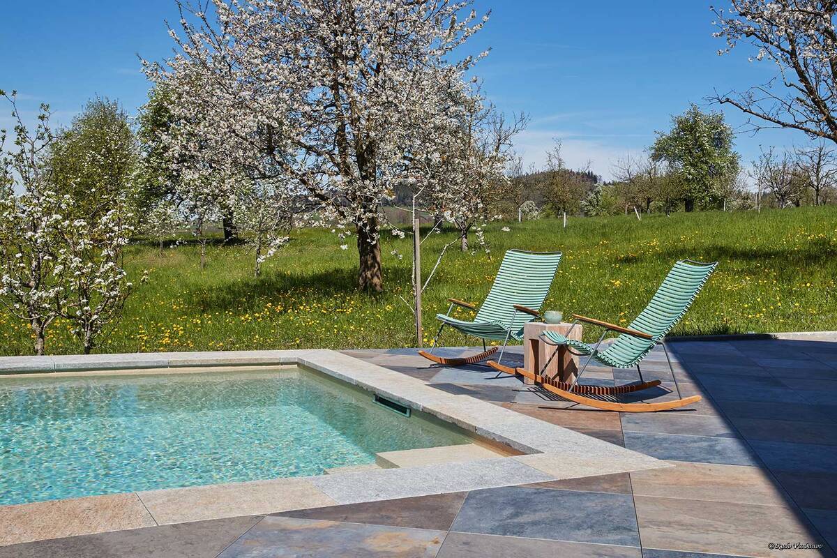 Das stilvolle Betonbecken, eingebettet in den Garten mit blühenden Obstbäumen, zeigt eindrucksvoll, dass ein Pool weit mehr sein kann als nur eine sommerliche Erfrischung. Der 10 × 3,30 × 1,50 Meter grosse Skimmer-Pool überzeugt mit hochwertiger Ausstattung: Die edle Folie Alkorplan Touch Relax, sechs Düsen und drei Unterwasserlampen sorgen für Komfort und stimmungsvolles Licht. Für optimale Wasserqualität sorgt eine moderne Salzaufbereitung. Vitabad.