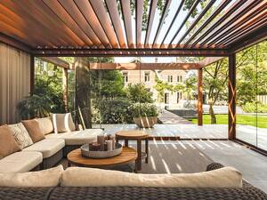 Die weichen Konturen in ruhigen Erdtönen und die natürlichen Materialien der Terrassenüberdachung wirken elegant und edel. Die klaren Linien strahlen Ruhe aus. Glasschiebetüren, Beleuchtungsarmaturen und faltbare Loggia-Paneele vervollständigen das Bild. Renson.