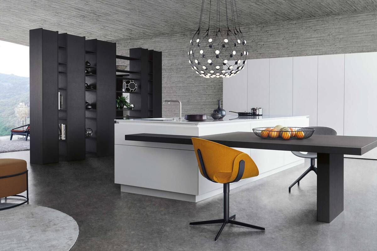 Der grifflose Inselblock und der in dunklem Holz gehaltene Sitzbereich verschmelzen elegant miteinander. Ein durch offene und geschlossene Regal- und Schrankeinschübe untergliedertes Element kommt als Raumteiler zum Einsatz. Foto: Leicht Küchen AG. Dipl. Ing. Fust.