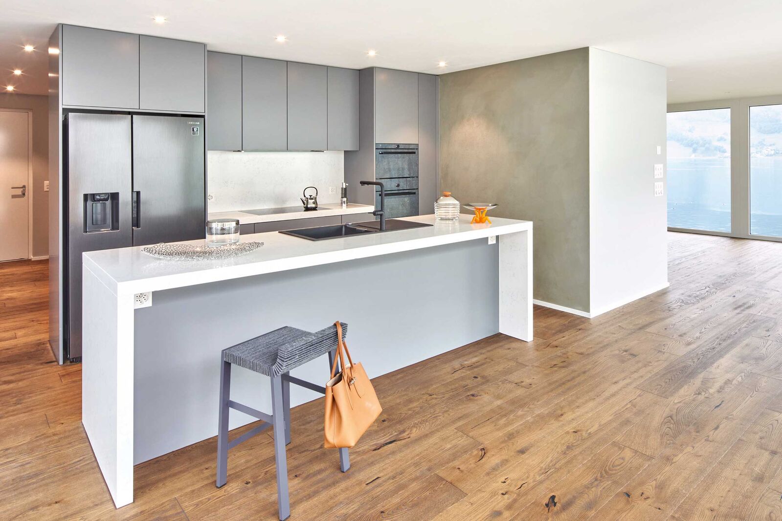 Schlicht und elegant, funktional und ästhetisch ansprechend: Die grau lackierten Fronten der marmorierte Kunststein, die schwarzen Griffleisten und der Holzboden schaffen bei der Küche «Colora laccato» eine wohnliche Atmosphäre.